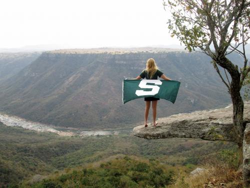 student with MSU flag on cliff